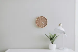 all white working space with round clock on the wall; plant and lamp on table